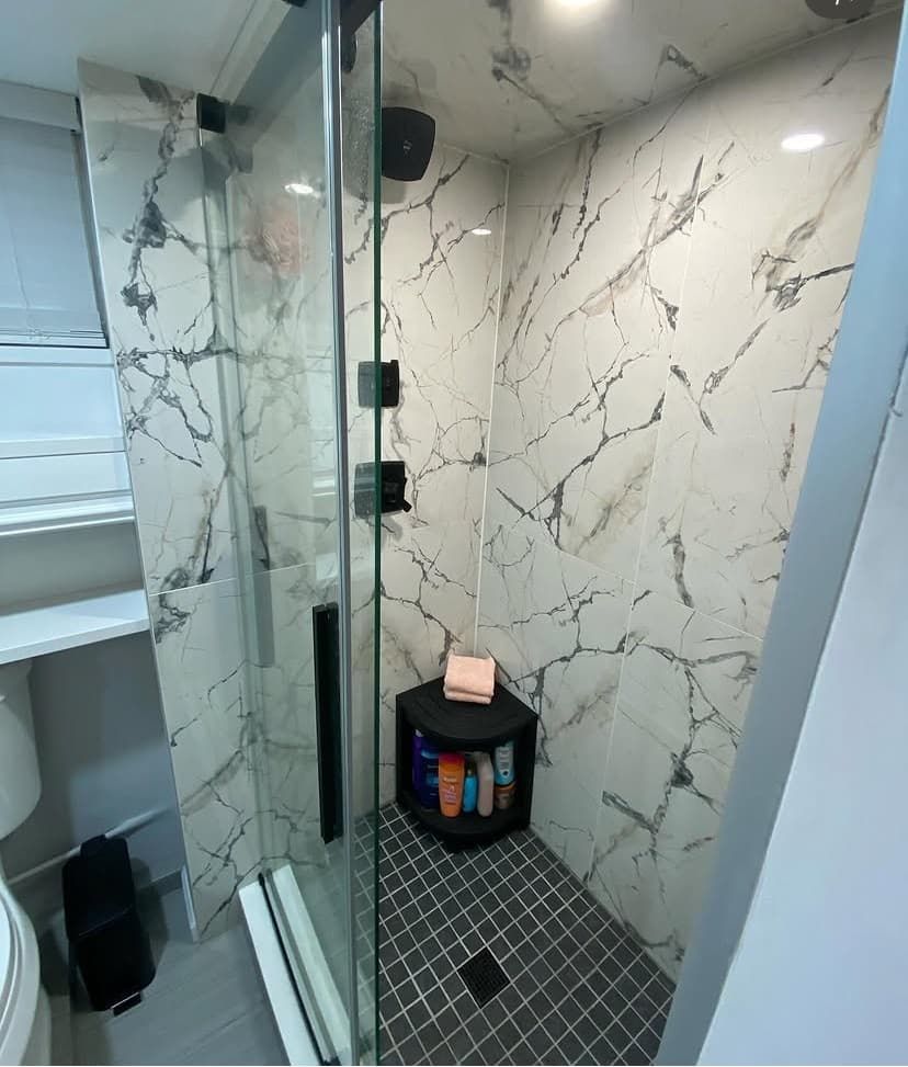 Walk-in shower with dramatic book-matched marble walls, black mosaic floor, and frameless glass door