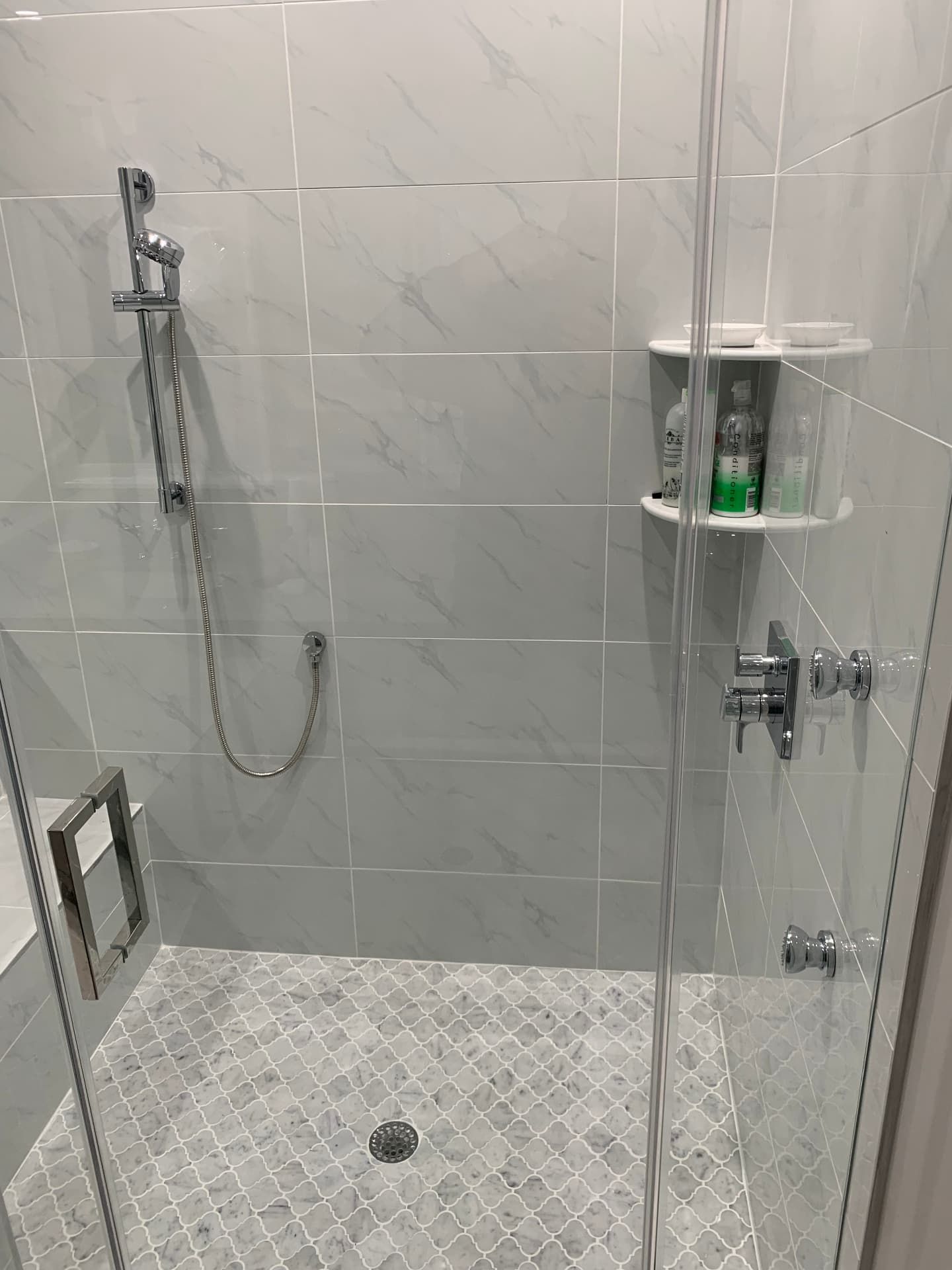 Marble-tiled shower with arabesque mosaic floor and chrome handheld fixture