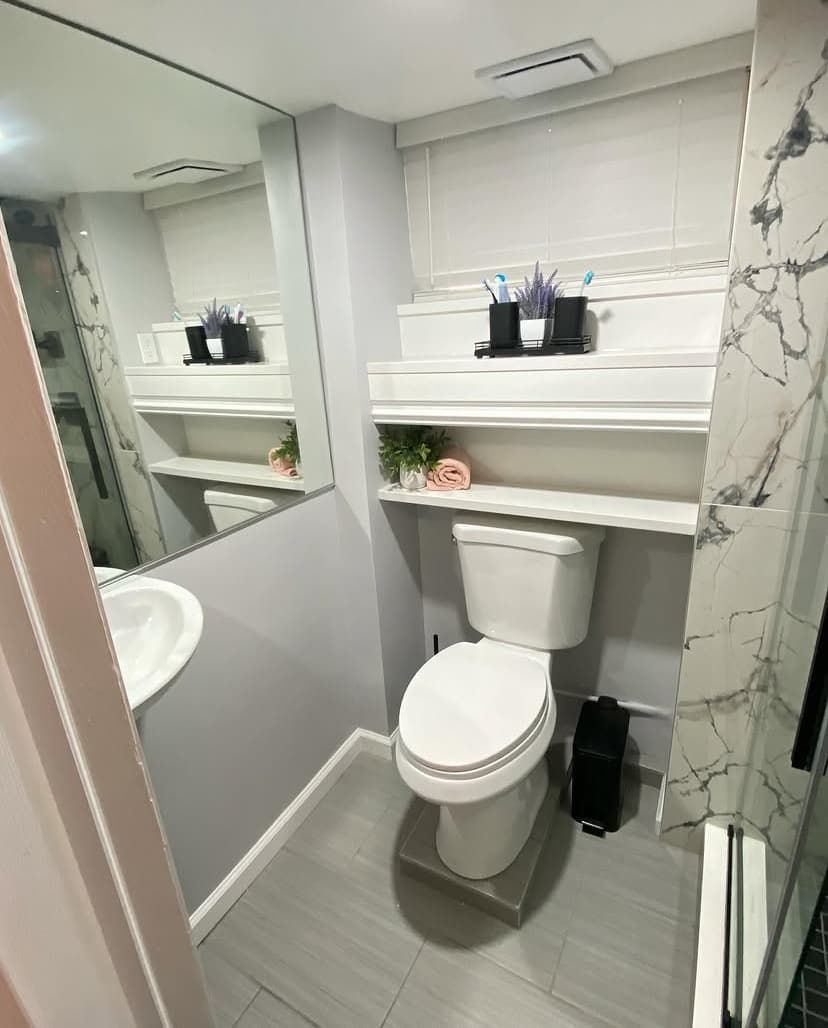Compact basement bathroom with marble shower, floating shelf, and gray plank tile floor