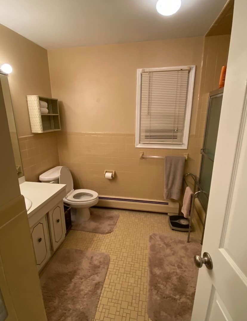 Dated beige bathroom with old vanity, tile, and yellow flooring before remodel