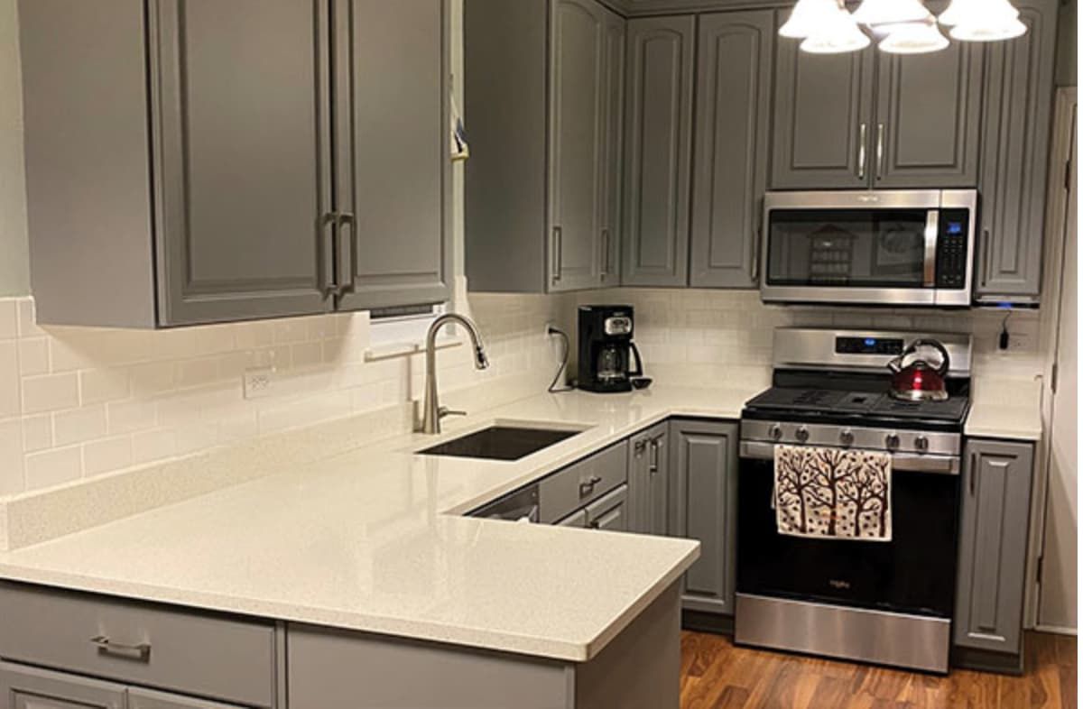 Refinished gray cabinets with white quartz counters and subway backsplash