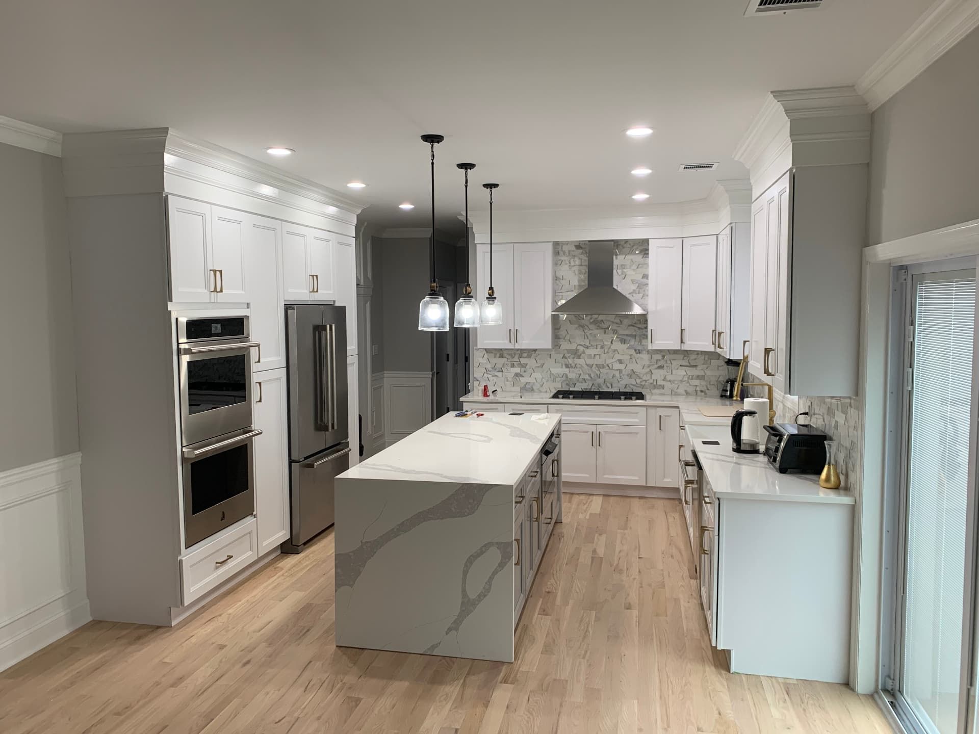 Bright white shaker kitchen with quartz waterfall island and brass pendants
