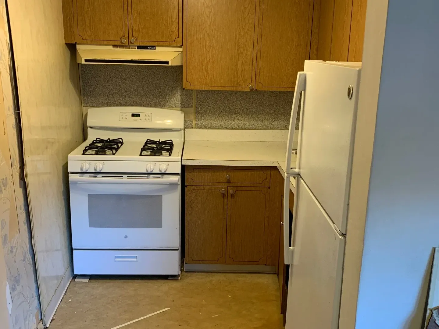 Dated galley kitchen with old cabinets and white appliances before remodel